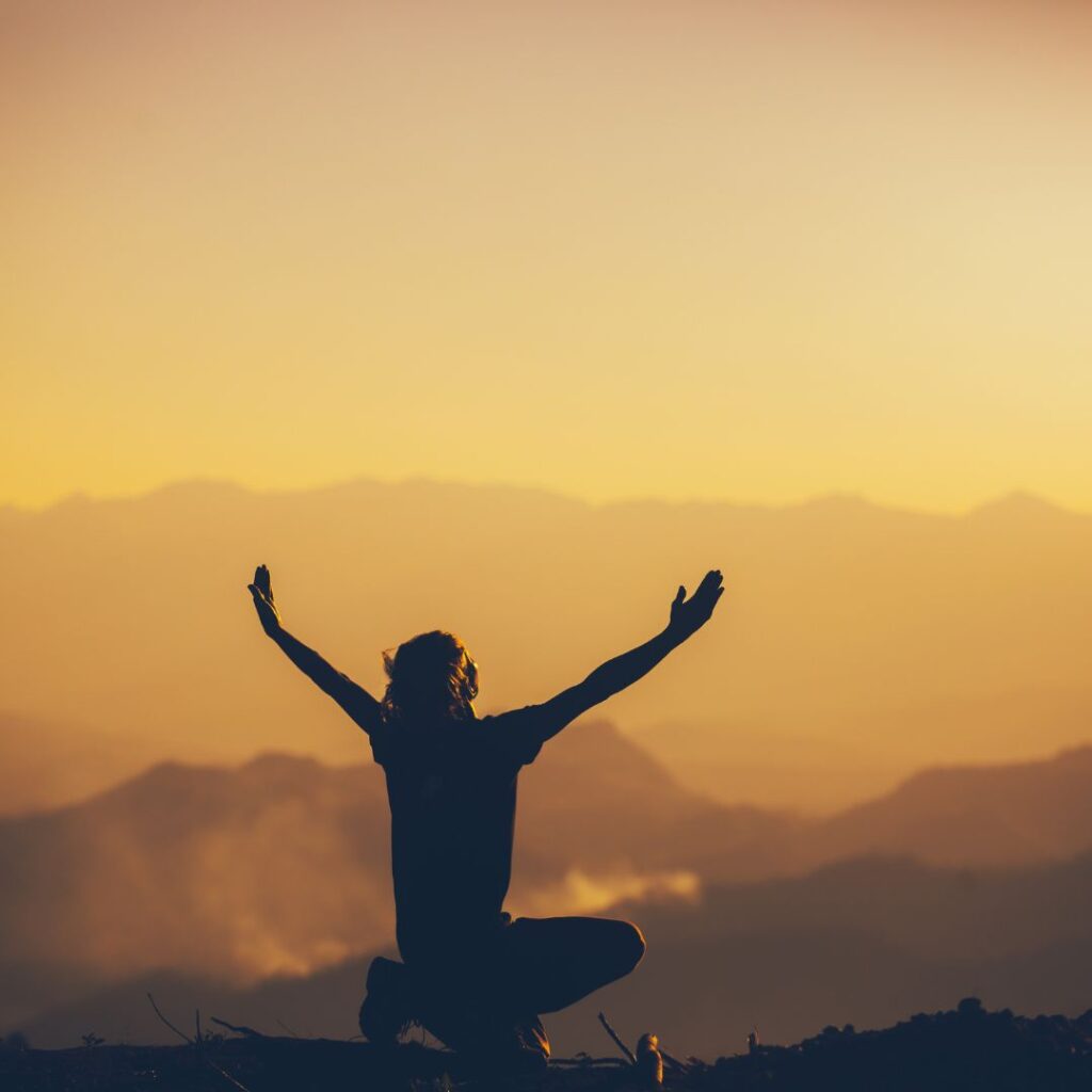 person raises their hands on a mountaintop 